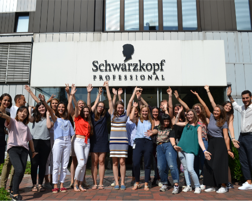 Un variegato team Henkel in piedi davanti all'edificio professionale di Schwarzkopf e alza le braccia