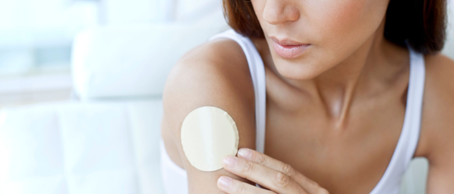 A young woman attaches a smart health patch to her right upper arm.