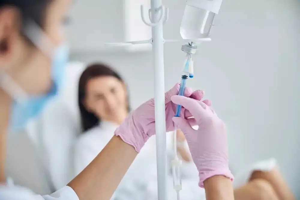Un operatore sanitario tiene in mano una sacca per flebo in un ambiente sanitario.