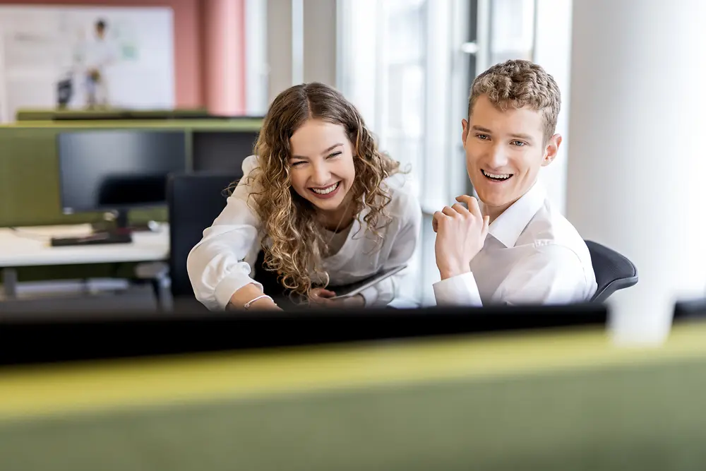 Due giovani professionisti che collaborano seduti a una scrivania in un moderno ambiente d'ufficio, a rappresentare i lavori per studenti e le posizioni di livello base.