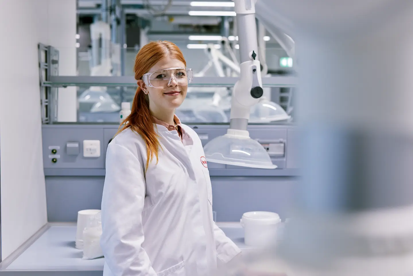 Laureato che inizia la sua carriera in Henkel, con indosso un camice bianco, in piedi in un moderno ambiente di laboratorio con attrezzature tecniche sullo sfondo.