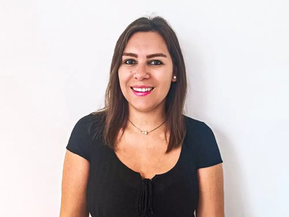Un recruiter in piedi davanti a uno sfondo bianco, con una maglia nera e una cintura beige, che condivide consigli su come gestire le domande difficili durante un colloquio.
