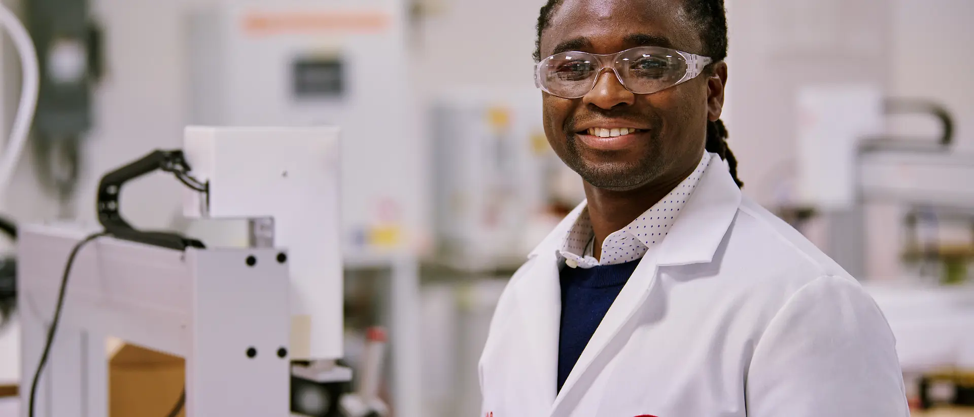 Una persona indossa un camice da laboratorio Henkel ed è ritratta in un ambiente di laboratorio, circondata da attrezzature e macchinari. Un contesto che richiama competenza scientifica, ricerca e innovazione.